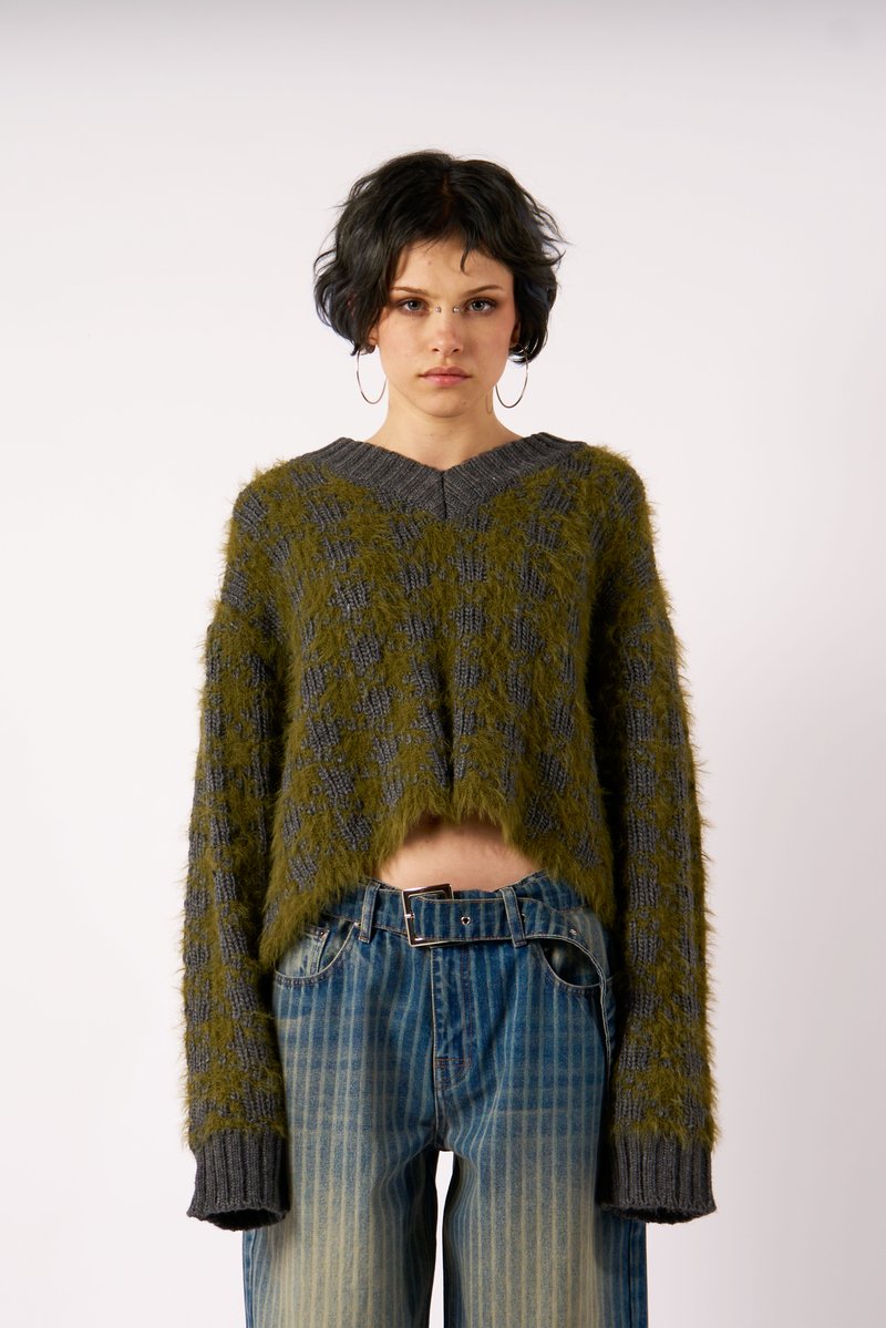 Vihreä ja harmaa lyhyt neulepusero, jossa on tekstuurinen kuvio, pitkät hihat ja V-pääntie, yhdistettynä sinisiin raitaisiin leveälahkeisiin farkkuihin.