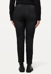 Pantalones de mezclilla negros con un corte ajustado, cinturilla elástica y dos bolsillos traseros. Llevados con botas negras hasta el tobillo, mostrados desde la parte posterior.
