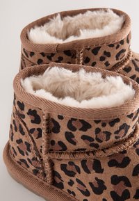 Ghete maro cu imprimeu leopard, cu căptușeală bej moale și pufoasă și detalii cusute. Exteriorul este realizat dintr-un material cu textură asemănătoare pielii întoarse.