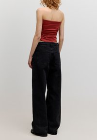 Schwarze weite Jeans mit hoher Taille, ausgestattet mit Gesäßtaschen, kombiniert mit einem enganliegenden, trägerlosen top in Rostfarbe.