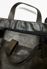Mörk l�äder tote-väska med två handtag, som har en texturerad yta. Inuti finns en subtil präglad logotyp på ett rektangulärt läderfack.