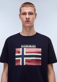 Marineblå bomulds t-shirt med et stort norsk flagg grafik i rød og blå design, og "NAPAPIJRI" trykt ovenfor i hvid.