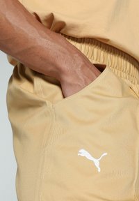 Gelbe Sportshorts mit einem elastischen Bund, Seitentasche und einem weißen Puma-Logo. Der Stoff hat eine glatte Textur mit einem subtilen Glanz.
