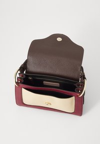 Sac à main en cuir avec un rabat supérieur marron, un corps bordeaux et une poche avant blanche cassé. Comprend des accessoires en or et plusieurs compartiments intérieurs.