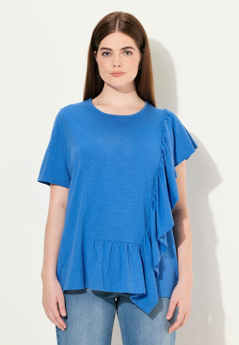Modrý krátký rukáv top s volánovým detailem na jedné straně, kulatým výstřihem a uvolněným střihem s nařaseným lemem. Měkká textilie.