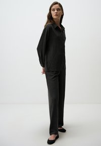 Ensemble de pyjama noir texturé comprenant une chemise à col et boutons et un pantalon droit, associé à des ballerines noires. Design simple et moderne.