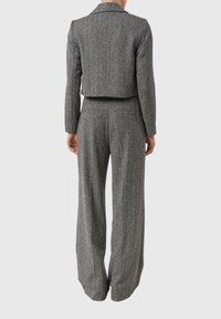 Szary garnitur w jodełkę, składający się z krótkiej marynarki z kołnierzem z wycięciem oraz spodni o szerokich nogawkach, wykonany z fakturowanej tkaniny.