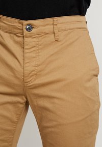 Pantaloni in cotone beige con chiusura a bottone, design a gamba dritta e superficie liscia, con dettagli di cucitura visibili sulle cuciture.