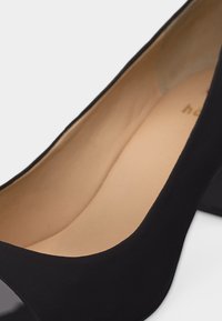 Fekete magas sarkú cipő lekerekített orral és bézs bélésbelsővel, közeli, szögből készült nézetben.
