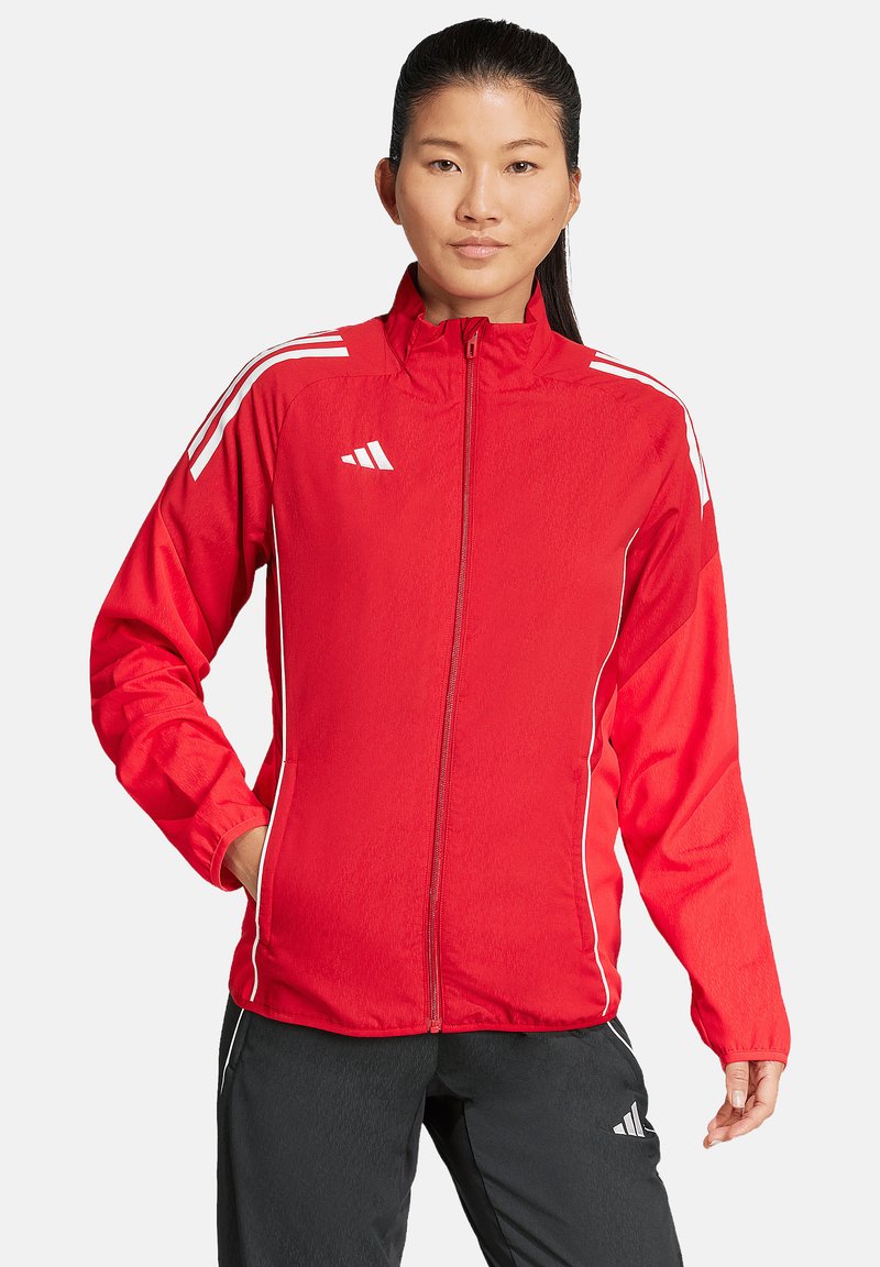 Rote leichte Jacke mit durchgehendem Reißverschluss, weißen Streifen auf den Schultern und seitlichen Taschen. Hergestellt aus glattem, atmungsaktivem Stoff.