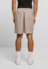 Beige, leichte Shorts mit einem elastischen Bund und einer einzelnen Gesäßtasche; knöchellang, glatte Textur, kombiniert mit weißen Sneakers und Socken.
