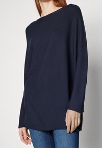 Haut à manches longues bleu marine en texture côtelée, avec un col bateau, une coupe décontractée et un ourlet arrondi. Associé à un jean en denim.