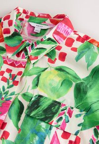 Rövid ujjú ing élénk virágos mintával, zöld levelekkel, rózsaszín és piros kiemelésekkel, könnyű anyagból készült, hegyes gallérral.