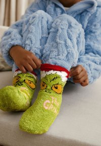 Zielone pluszowe skarpetki z wzorem postaci Grincha o żółtych oczach i różowym napisie. ściągacz w czerwono-białe paski; miękka tekstura.