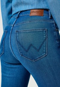 Vaqueros de mezclilla azul con un acabado texturizado, que presentan una etiqueta de cuero marrón y una costura en zigzag distintiva en los bolsillos traseros.