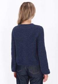 Granatowy sweter dzianinowy z teksturowanym prążkowanym wzorem, okrągłym dekoltem i długimi rękawami, w połączeniu z niebieskimi dżinsami.