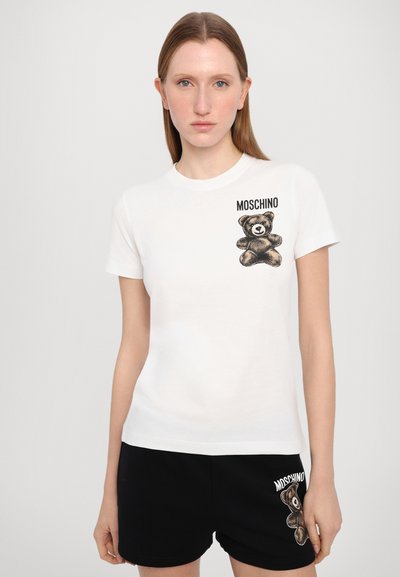 Baltos medvilnės marškinėliai su lokio grafika kairiajame viršutiniame kampe ir užrašu "MOSCHINO". Trumpi rankoviai ir klasikinis apvalus kaklas.