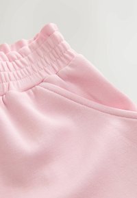 Pehme vaaleanpunainen kangas joustavalla vyötäröllä ja sivutaskulla, jossa näkyy yksityiskohtaiset ompeleet ja sileä pinta.