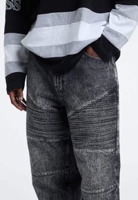 Pantaloni in denim larghi a due tonalità, neri e grigi. Presentano pannelli verticali a righe e testurizzati, aree consumate e un classico design a cinque tasche.