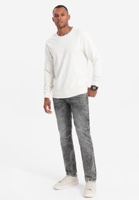 Valkoinen pitkähihainen collegepaita, harmaat kuluneet farkut ja vaaleat lenkkarit. Yksinkertainen muotoilu, jossa on ribbivaroja hihoissa ja kauluksessa; rento malli.