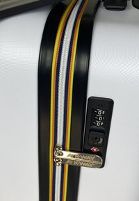 Valigia rigida bianca con cerniera nera, caratterizzata da una striscia multicolore e una combinazione di lucchetto con un tirazip in argento.