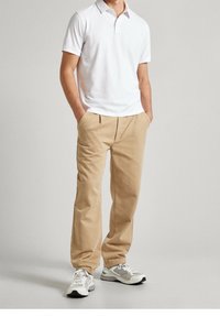 Męski strój składający się z białej koszulki polo i beżowych spodni z fałdami, połączony z szaro-białymi trampkami. Prosty, czysty design.