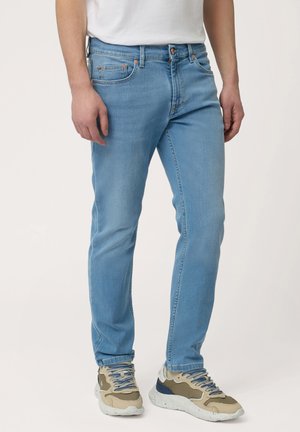Light blue jeans made of denim, featuring a straight leg design, five pockets, and copper-tone hardware details. Worn with beige and gray sneakers.