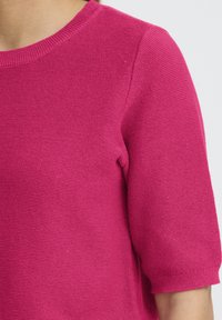 Fuksija pleteni top s okruglim izrezom, kratkim rukavima i teksturiranim materijalom. Rubovi rukava su rebrasti za tijesno prianjanje.