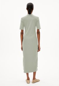 Langes, hellgrünes Kleid aus strukturiertem Stoff, mit kurzen Ärmeln und seitlichen Schlitzen, kombiniert mit beigen Slippern.