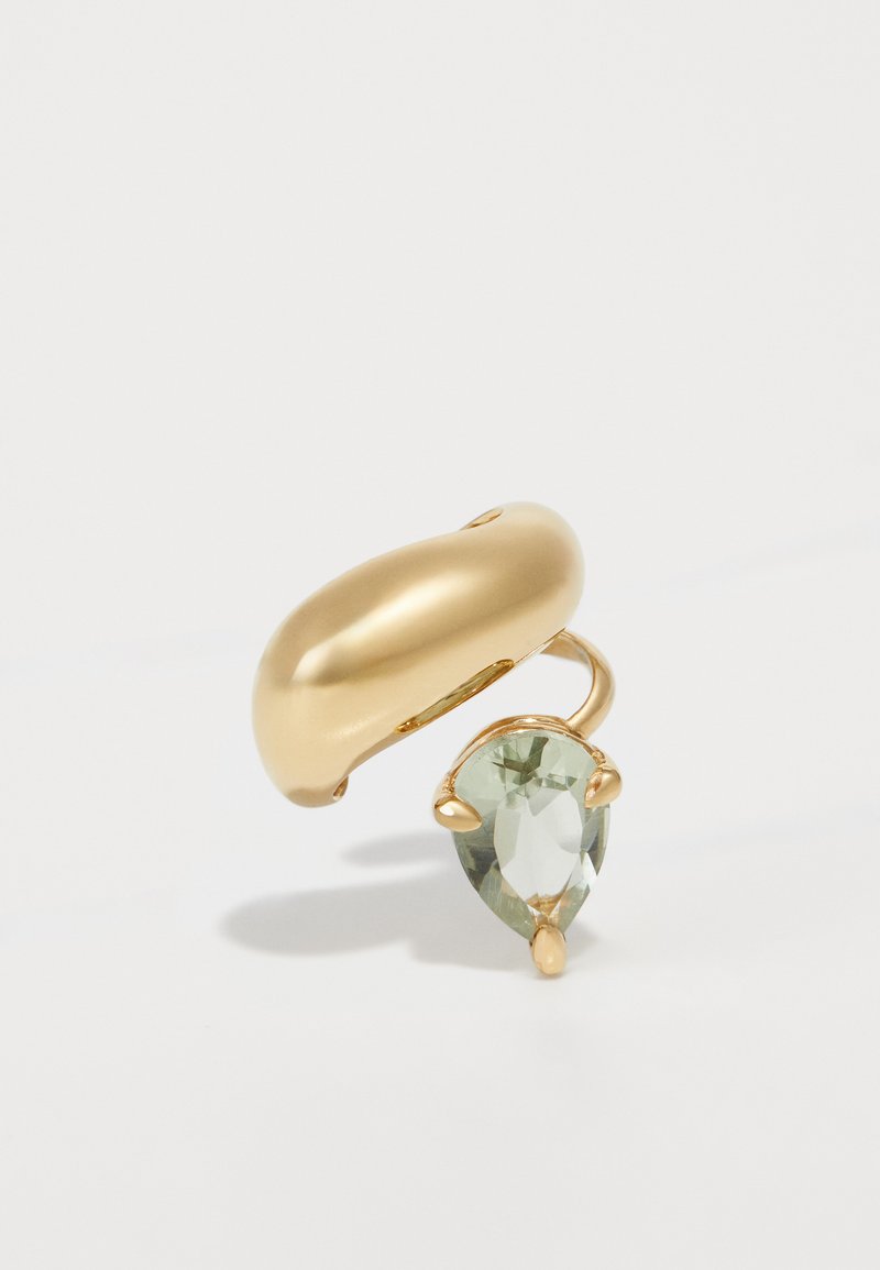Gold metal ring with a smooth, curved band and a pear-shaped green gemstone setting at one side. Polished finish, no visible patterns.
