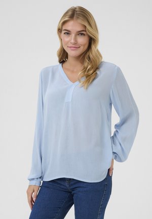 Blouse bleu clair à manches longues avec un décolleté en V, présentant une texture subtile et une coupe décontractée. Tissu lisse, poignets froncés et ourlet droit.