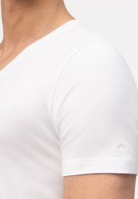 Witte korte mouwen V-hals t-shirt gemaakt van zachte katoen. Heeft een subtiele logo-detail op de mouw en een gladde textuur.