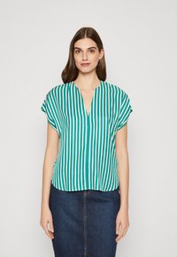Kortermet grønn bluse med vertikale hvite striper, V-hals-design, glatt tekstur, kombinert med en mørk denimskjørt.