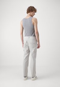 Pantalones cargo gris claro con múltiples bolsillos, tela de algodón, corte recto, combinados con una camiseta sin mangas gris y zapatillas blancas con acentos negros.