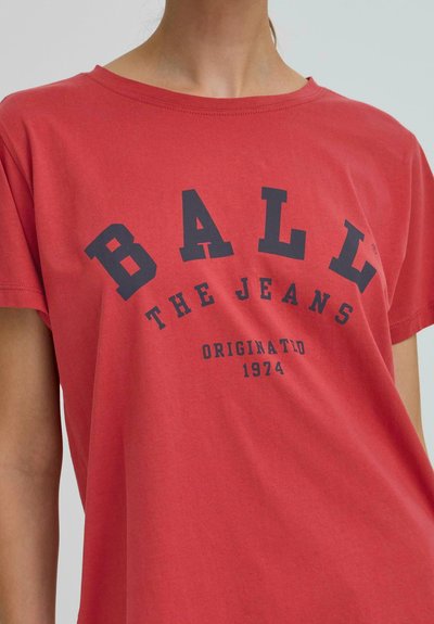 T-shirt en coton rouge avec un col rond et des manches courtes. L'avant présente un grand texte bleu marine : "BALL THE JEANS ORIGINAL 1974."