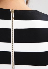Czarny i biały top w paski z gładką teksturą materiału, z centralnym zapięciem na zamek błyskawiczny z metalowym uchwytem.