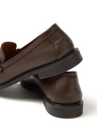 Brown leather loafers with a textured finish, featuring a curved design, low profile, and black rubber soles, showcasing subtle stitching details.