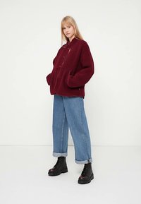 Bordo fliisist jakk luku ja suurete taskutega, lõdva istuvusega, kombineeritud helesiniste, lõtvade teksapükstega ja mustade saapadega.