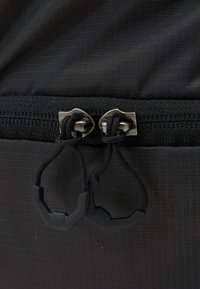 Černá látková taška na zip s dvojitými kovovými zipy s černými šňůrkami, zesíleným prošíváním a texturovaným vzorem na povrchu.