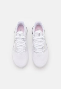 Bílé sportovní boty s texturovaným síťovaným svrškem, tenkými plochými tkaničkami a růžovým akcentem na stélce. Mají černou opěrku na patě pro podporu.