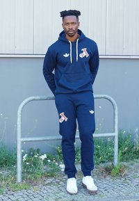 Mornarji kapuco in trenirke s vezenimi logotipi v rdeči in beli barvi, bele vezalke in detajli. Bele športne čevlje.