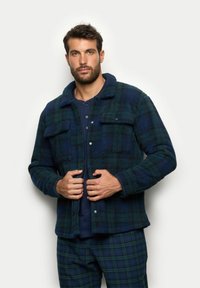 Giacca in pile a camicia nei toni del blu scuro e verde a quadri. Presenta una chiusura con bottoni, colletto e due tasche sul petto. Tessuto morbido.