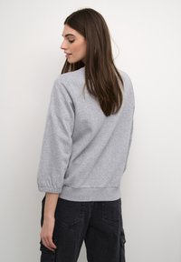 Felpa grigia in cotone con polsini e orlo a costine, caratterizzata da una vestibilità comoda e un design semplice, mostrata da dietro su uno sfondo chiaro.
