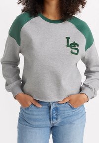 Sweat-shirt gris avec des manches raglan vertes et un logo "LS" brodé. Il présente une coupe courte avec des poignets et un col côtelés.