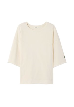 Tričko krémovej farby s okrúhlym výstrihom, krátkymi dolmánovými rukávmi a malým zeleným logom na ľavom rukáve. Mäkká, ľahká látka.