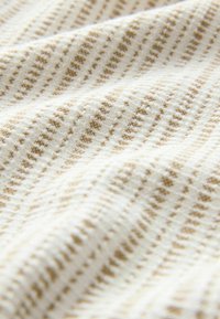 Karkea kangas kerma- ja beige-sävyissä, jossa on hienovarainen raidallinen kuvio pienten kohotettujen yksityiskohtien kanssa, luoden pehmeän, kosketeltavan pinnan.