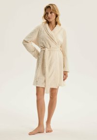 Kremowy haftowany szlafrok z kołnierzem typu szal, długimi rękawami i wiązanym pasem w talii. Miękka, teksturowana tkanina z delikatnym wzorem w romby.