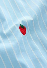 Tissu bleu clair avec des rayures blanches verticales, comportant un petit design de fraise rouge brodé avec des feuilles vertes.