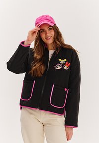 Čierna prešívaná bunda s ružovým lemovaním, s tromi karikatúrnymi nášivkami na hrudi a dvoma prednými vreckami. Nosená s ružovou čiapkou.