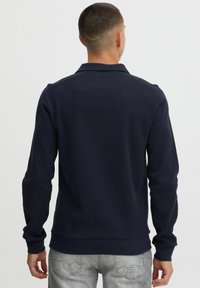 Sweatshirt tricot navy à manches longues, avec des poignets et un ourlet côtelés, doté d'un col et d'un tissu texturé. La vue arrière montre des détails minimaux.
